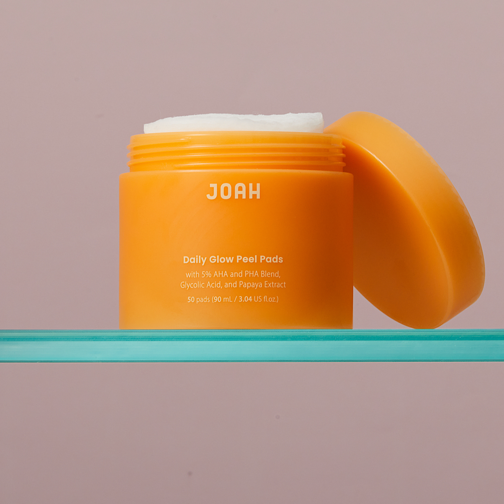 Orange jar of JOAH Daily Glow Peel Pads on a teal shelf with a pink background
