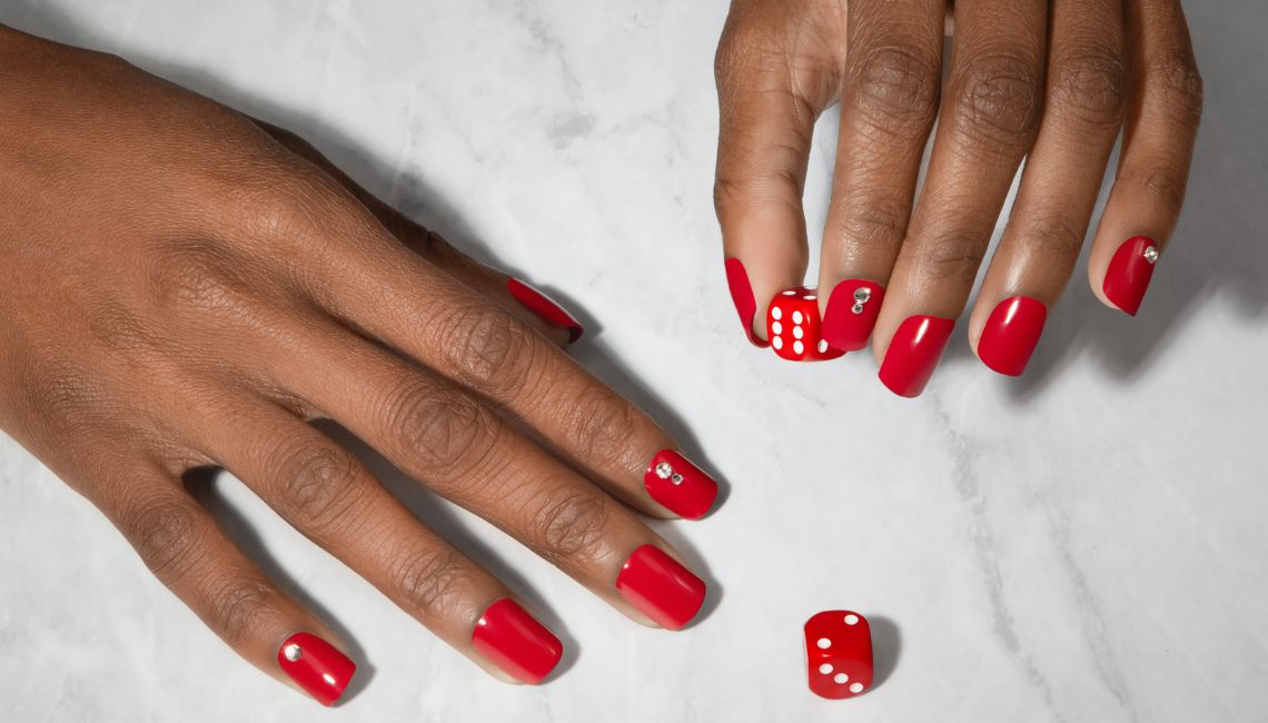 Red nails with dice on a marble background